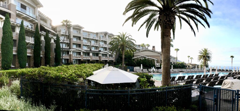 A hotel with palm trees and a pool in the background.
