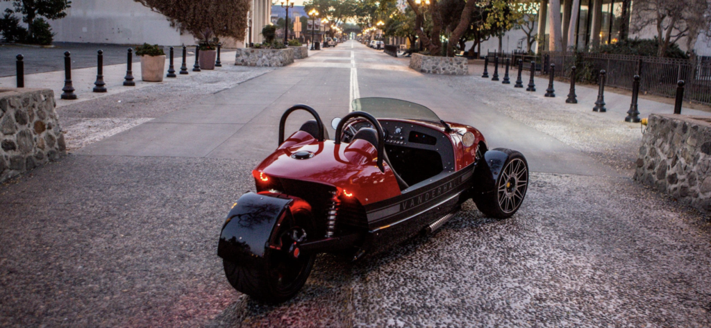 A red and black three wheeled motorcycle parked on the side of a street.