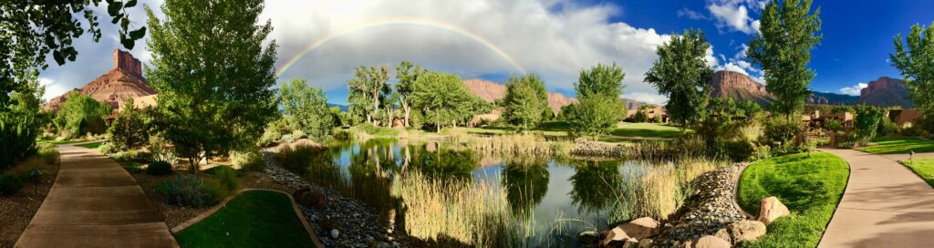 A rainbow over the water and trees in front of mountains.